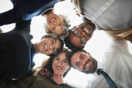 Diverse group of colleagues hugging in a circle and looking down to the camera smiling
